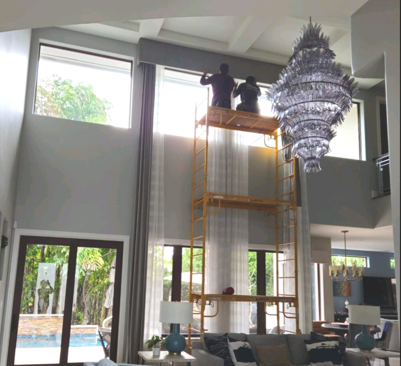 Two-story drapery installation on tall windows with a scaffold and chandelier